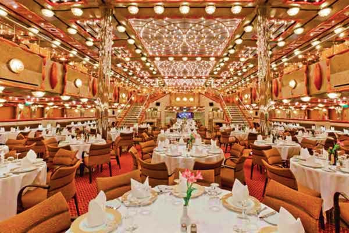 Elegant dining room on Costa Favolosa cruise ship with white tablecloths, tan leather chairs, ornate crystal chandeliers, and