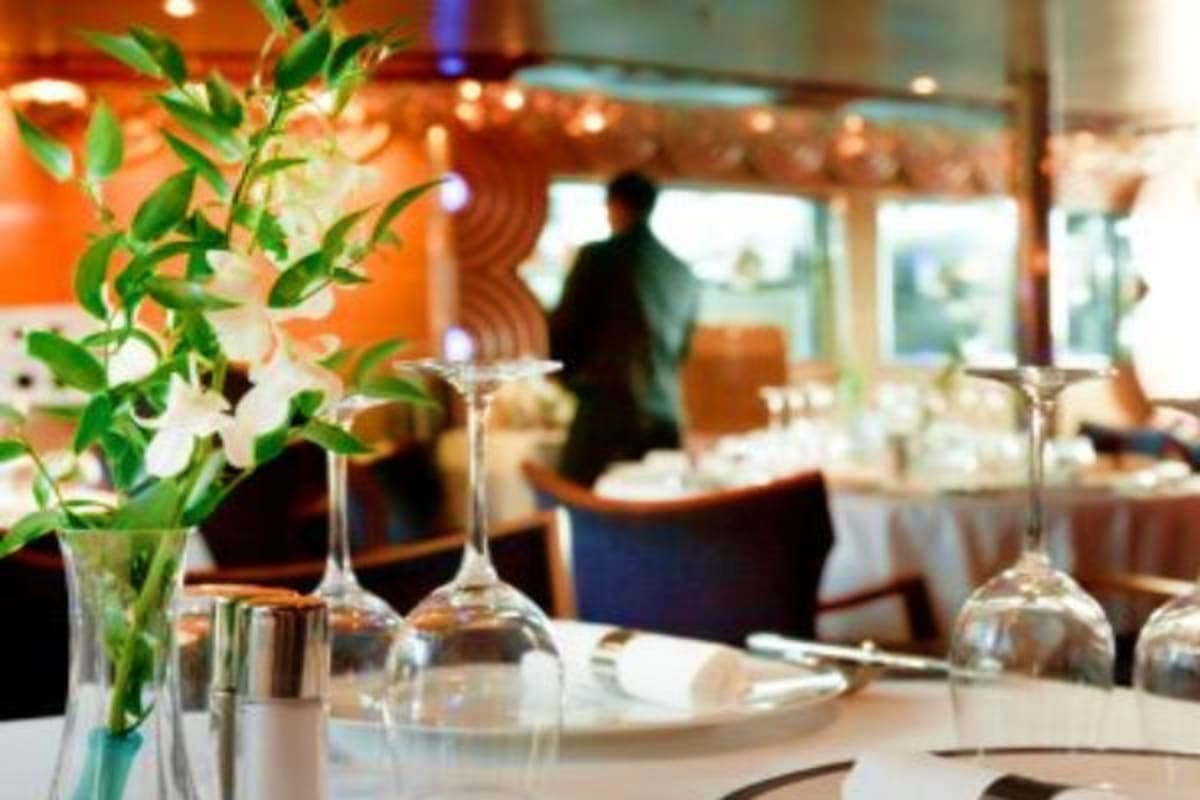 Fine dining restaurant table with white flowers and place settings, blurred server in background aboard cruise ship
