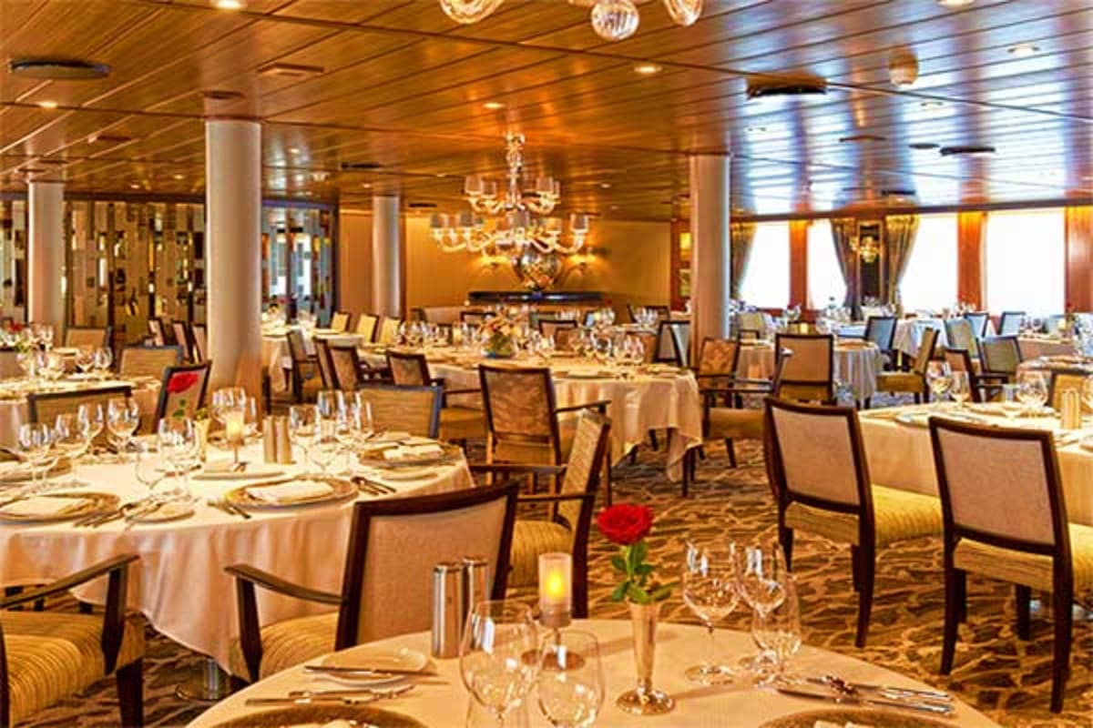 Elegant dining room on Wind Star cruise ship with round tables, formal place settings, crystal chandelier, and ocean views th