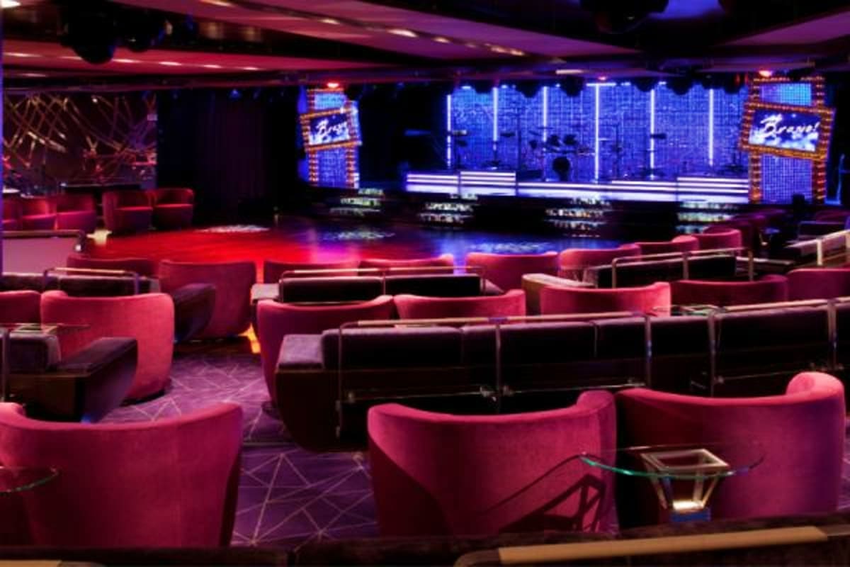 Modern nightclub interior with pink curved seating, blue neon lighting, dance floor, and stage with digital displays