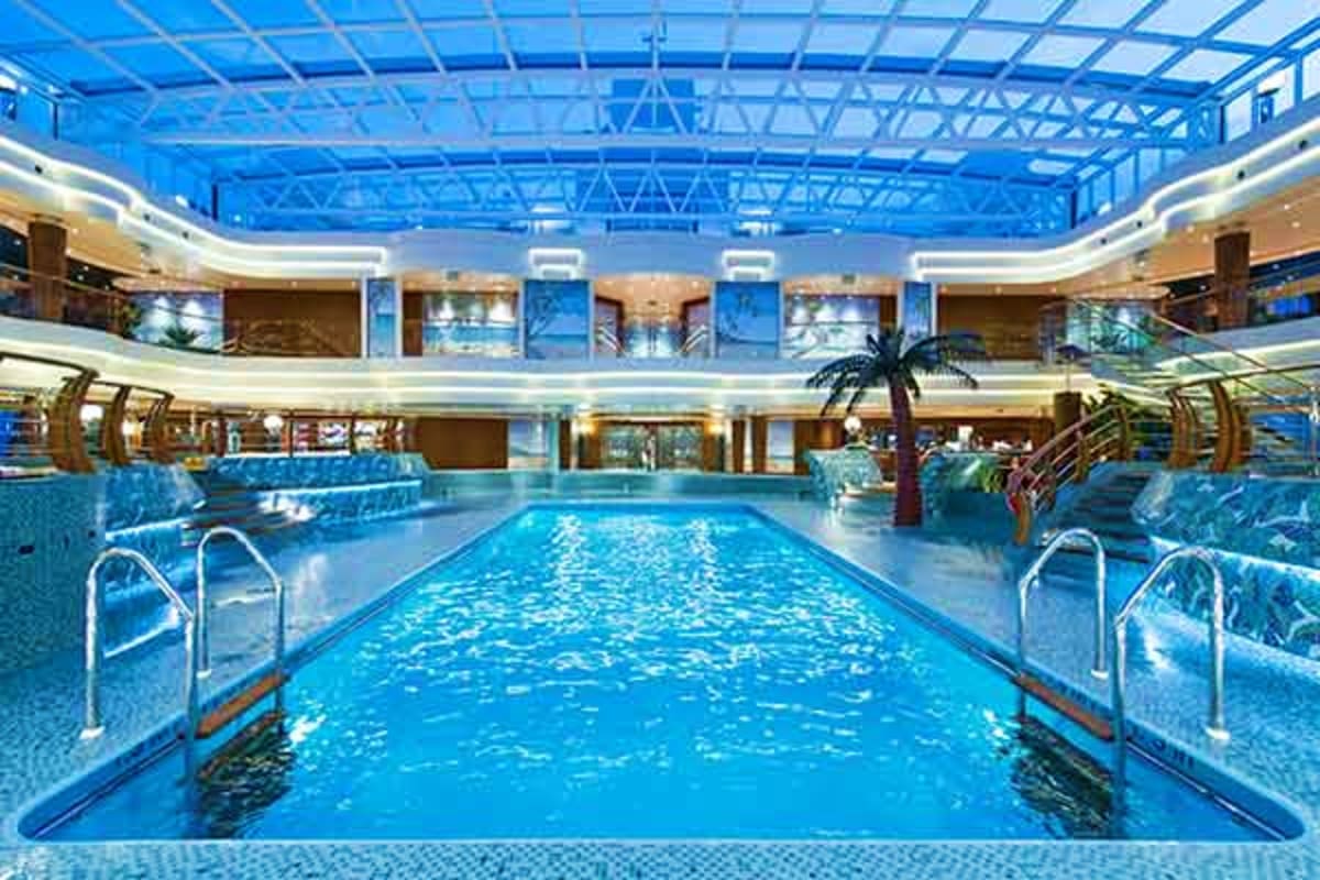 Indoor swimming pool with blue water and metal railings on MSC Preziosa cruise ship, multi-level atrium with glass ceiling