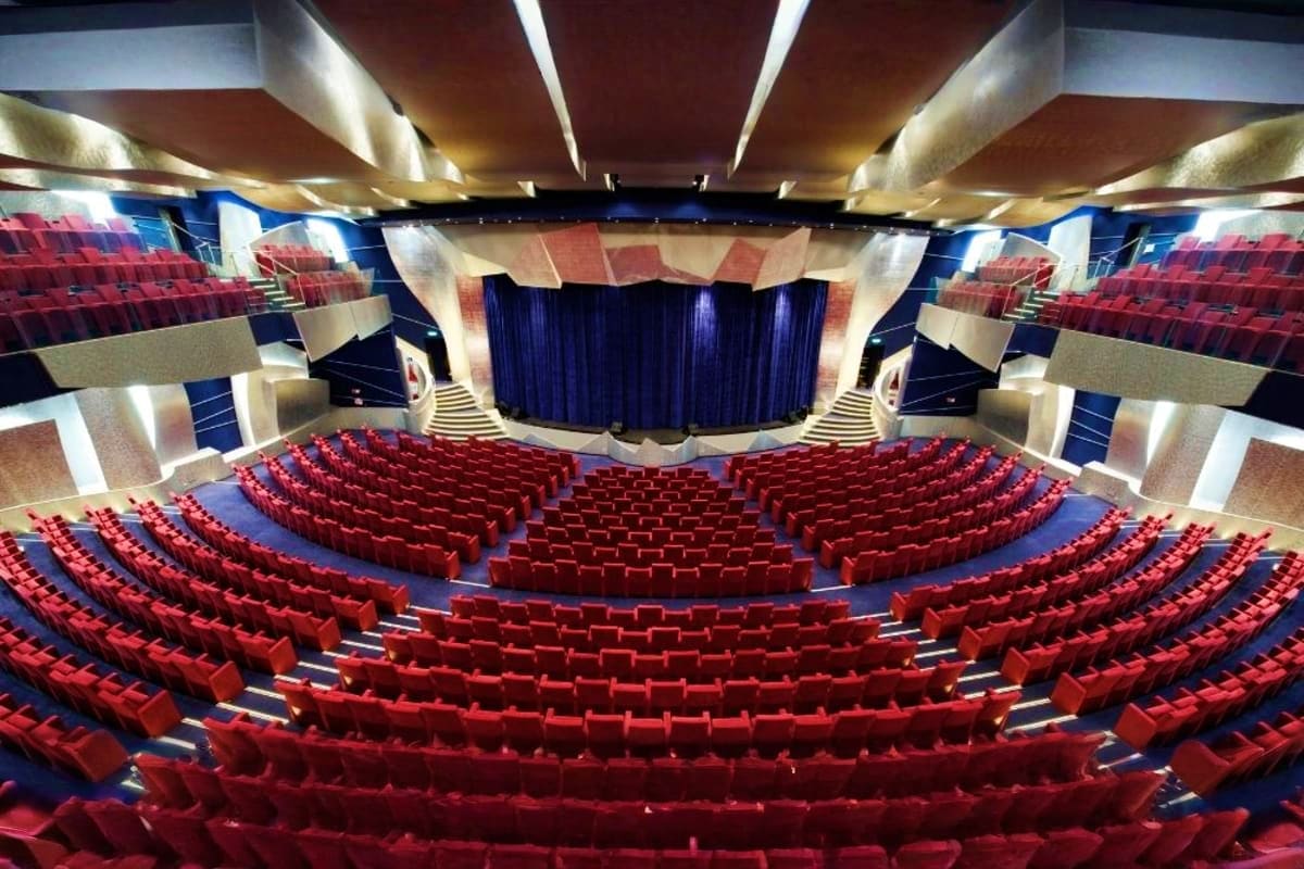 Modern theater interior with rows of red seats facing a stage with blue curtains and illuminated ceiling design