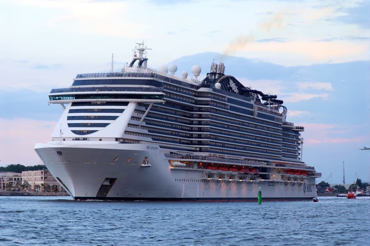 Large modern cruise ship MSC Seaview anchored in blue ocean waters with mountains and coastal buildings visible in background
