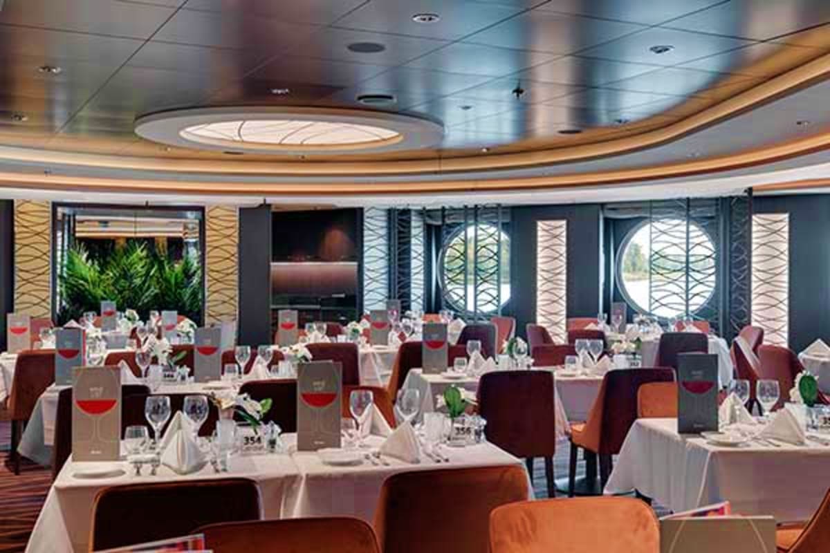 Formal dining room on MSC Seaview cruise ship with white tablecloth tables, burgundy chairs, place settings, and large curved