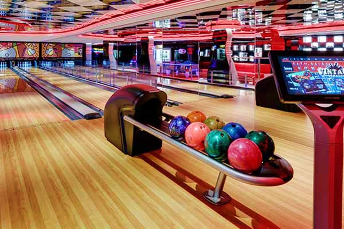 Modern bowling alley interior with colorful bowling balls on automatic ball return system and wooden lanes