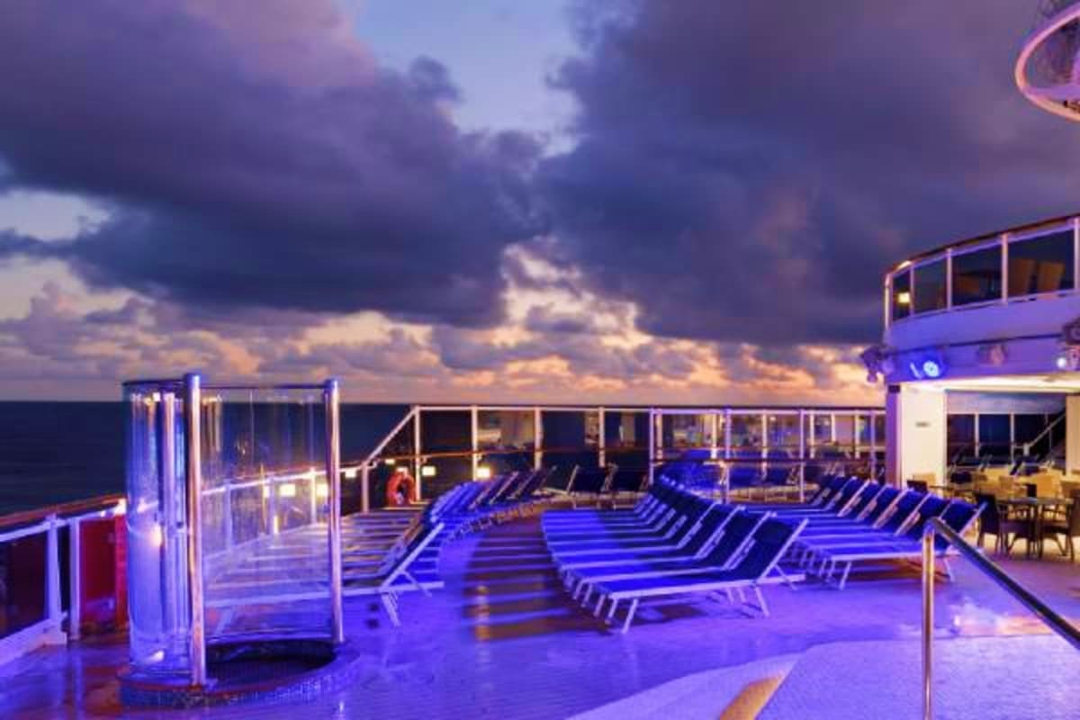 Cruise ship deck at dusk with rows of blue lounge chairs, ocean view, and dramatic cloudy sky above