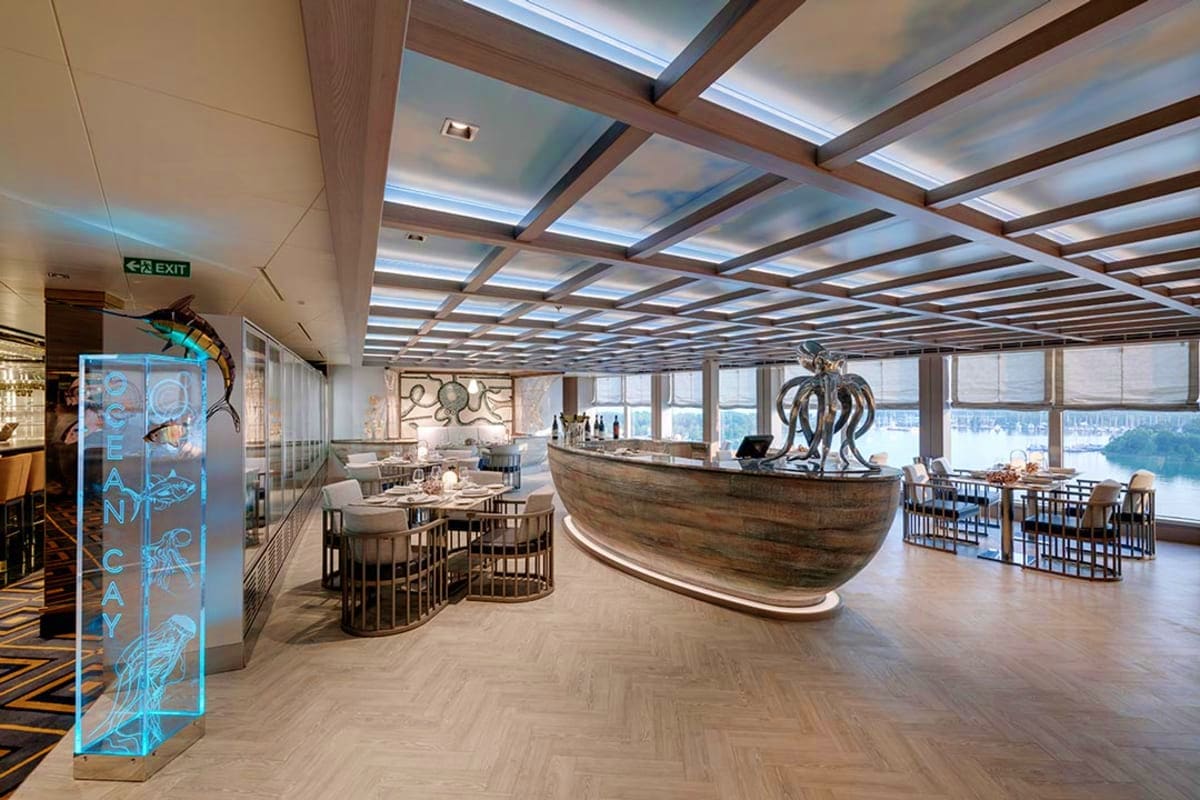 Modern cruise ship dining area with octopus sculpture centerpiece, floor-to-ceiling windows overlooking ocean, and skylight c