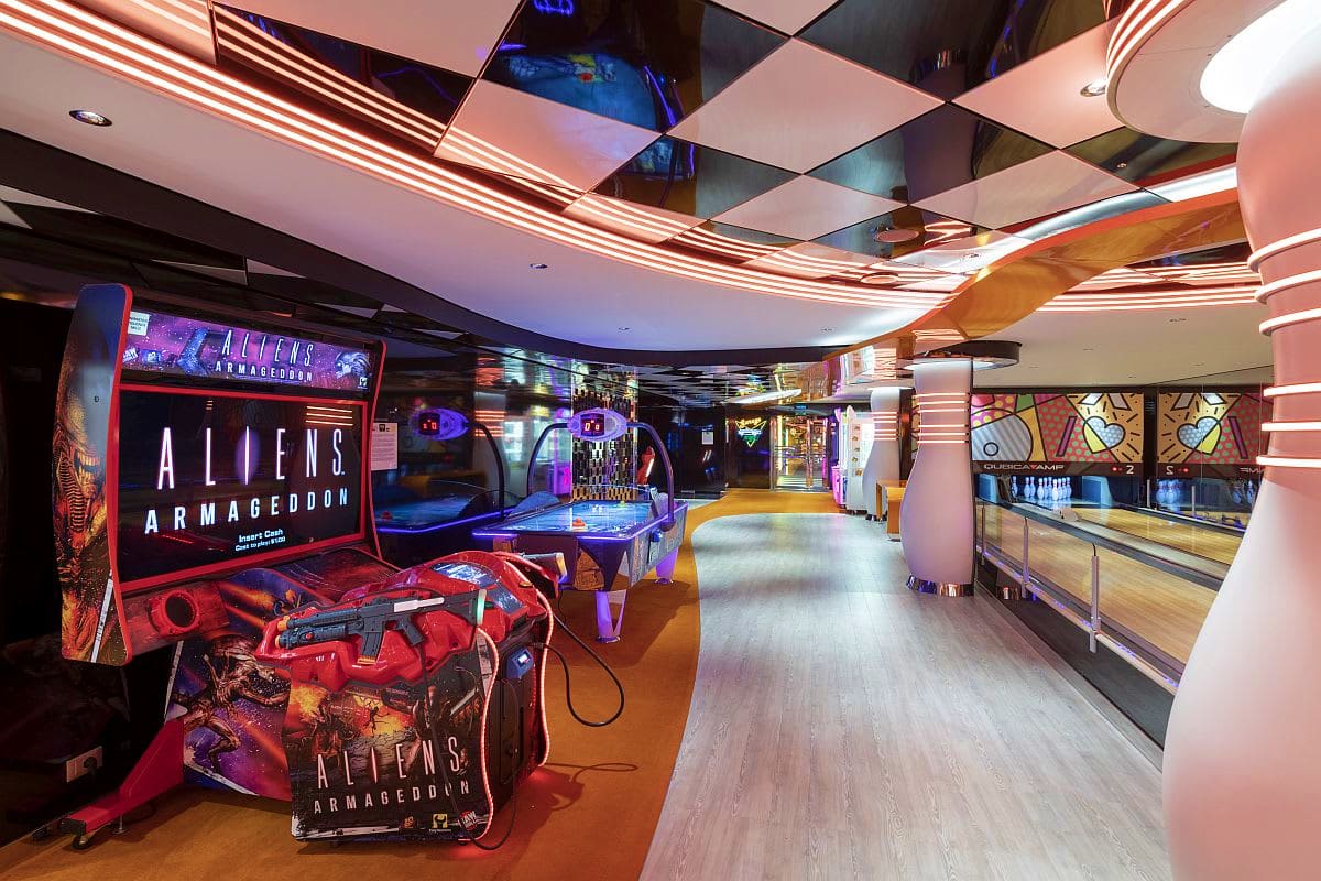 Modern arcade room on MSC Seaview cruise ship with neon red Aliens Armageddon game cabinet, bowling lanes, and colorful LED c