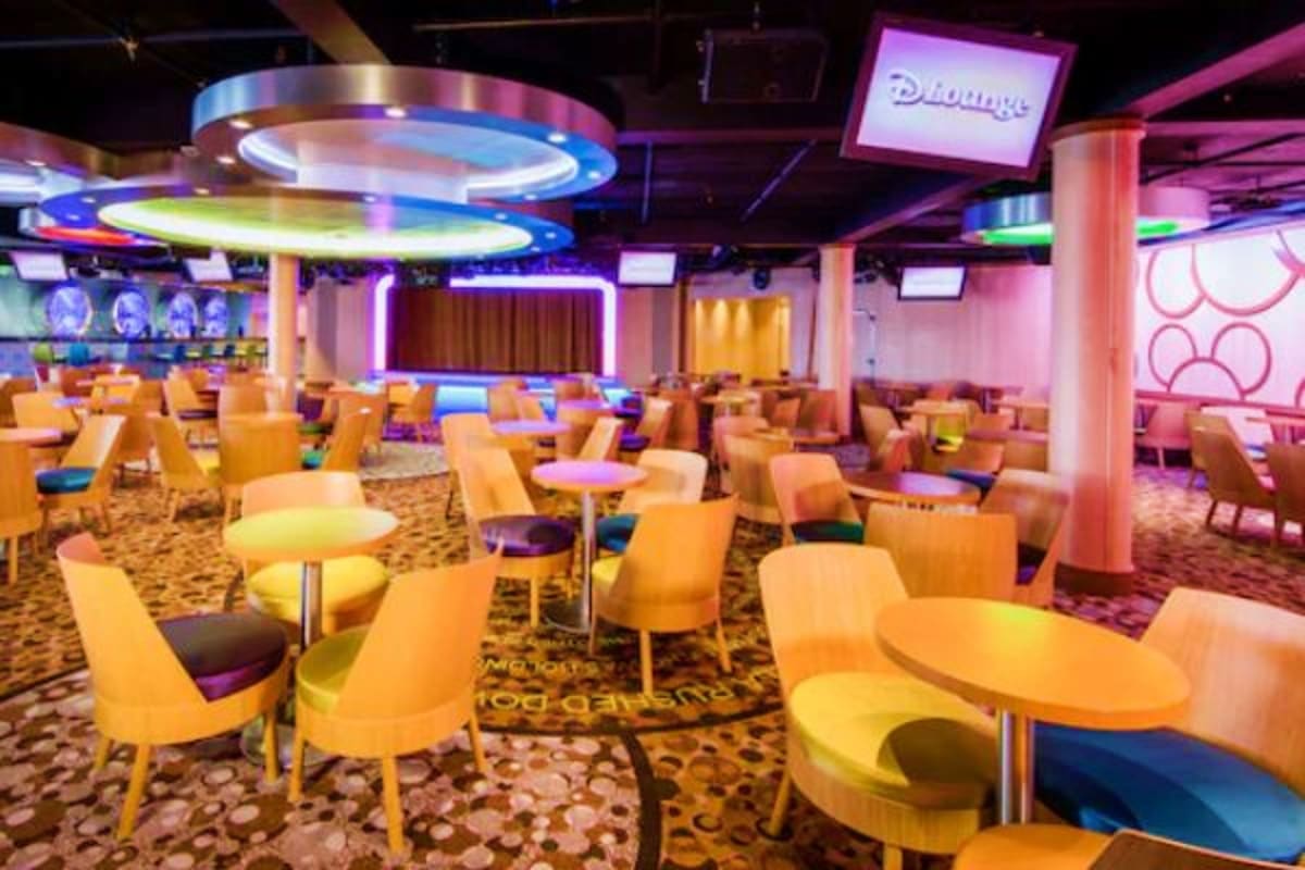 Magical Asia Cruise Escape Modern cruise ship lounge with colorful neon lighting, orange chairs, round tables, and blue accent lighting on ceiling fixtu