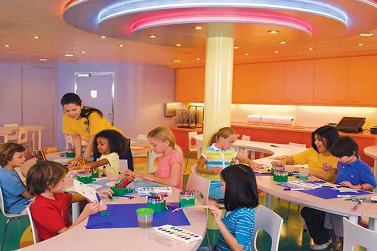 Children participating in an art and craft activity in a brightly lit, modern onboard classroom with colorful walls and neon