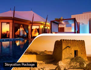 Ras Al Khaimah Heritage Escape with City Tour and Desert Safari Luxury beachfront villa at sunset with illuminated pool overlooking Arabian Gulf, adjacent to historic desert fort tower in R