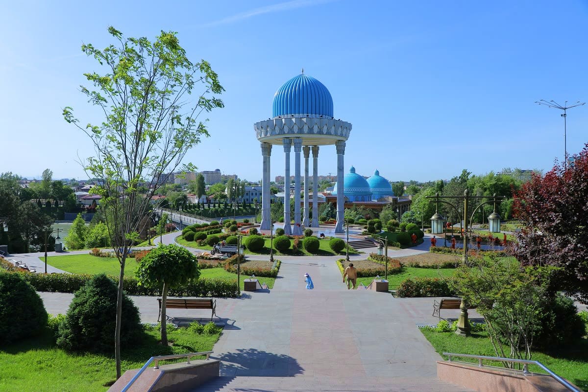 Uzbekistan Silk Road Journey Central Asian plaza with blue-domed pavilion, manicured gardens, and tree-lined pathways under clear sky