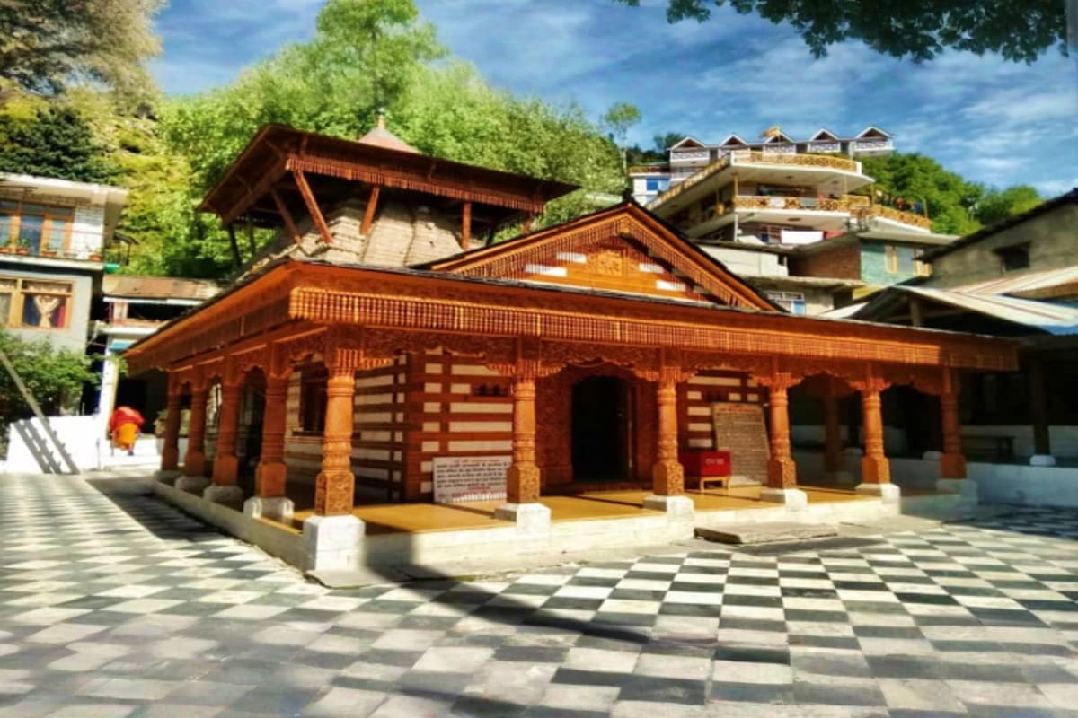 Traditional wooden temple with red and white striped architecture in Manali, surrounded by green trees and mountain buildings