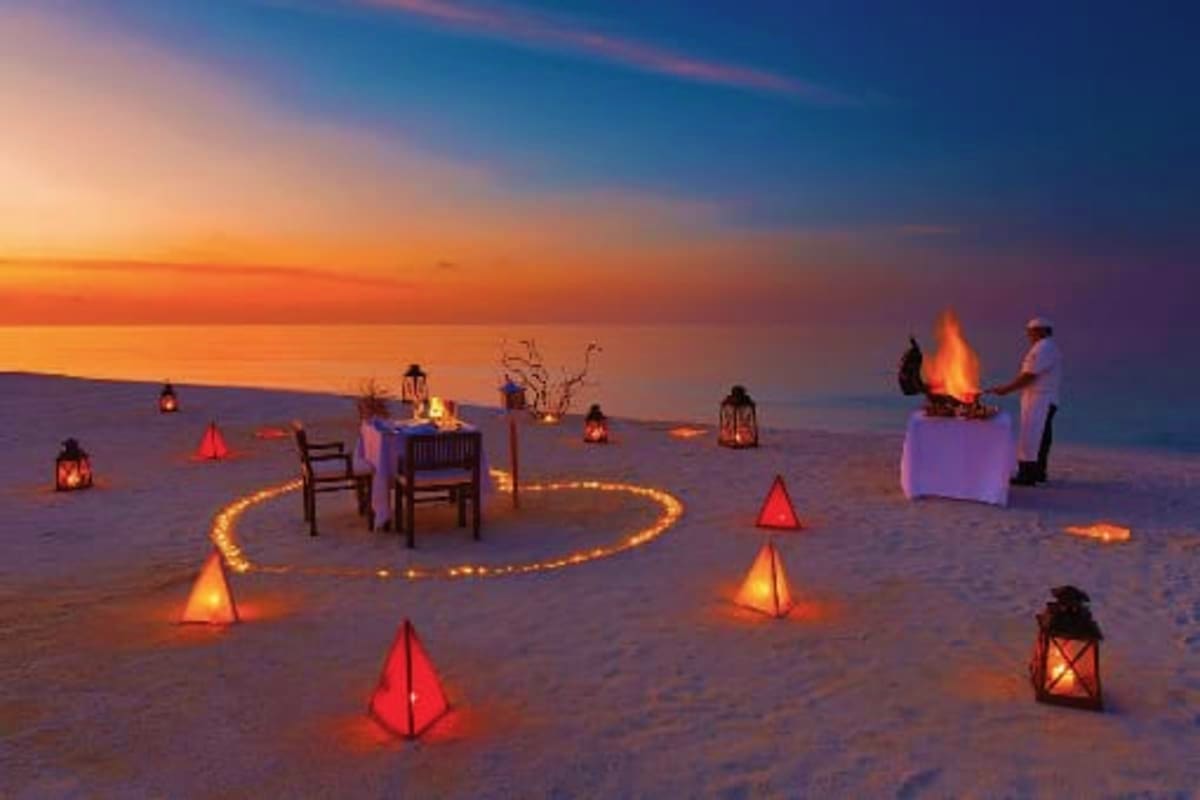 Bali Premium Island Retreat Romantic beach dinner setup at sunset with glowing lanterns, candles, and decorative lights arranged on sand during twilight