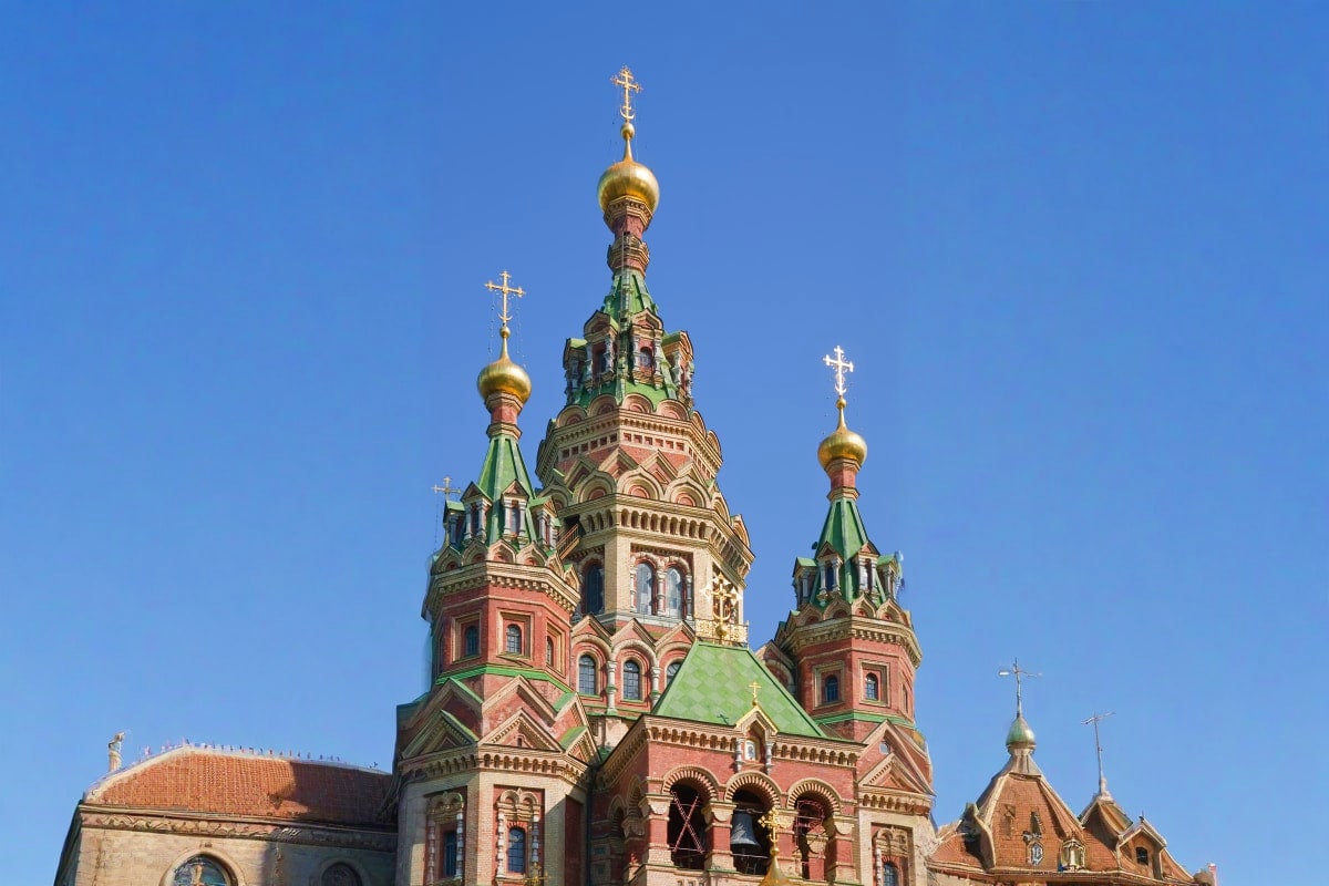 Russian Orthodox church with golden onion domes and ornate spires against clear blue sky in Kazakhstan