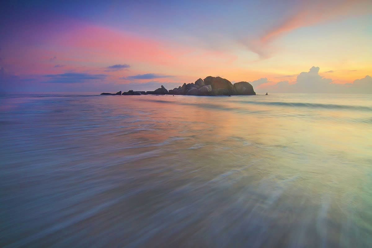 Rocky granite outcrops and turquoise waters at sunset in Seychelles, with smooth waves from long exposure photography