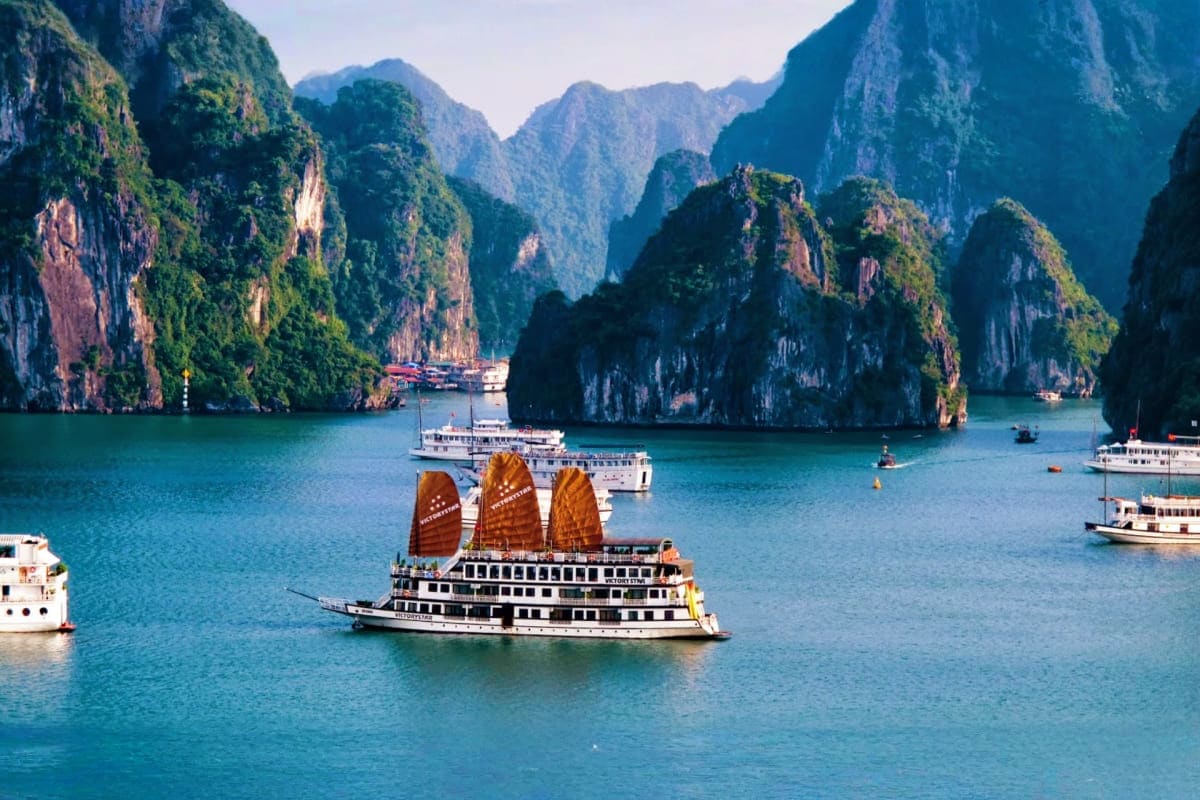 Traditional junk boat with golden sails in turquoise waters surrounded by limestone karst cliffs in Halong Bay, Vietnam