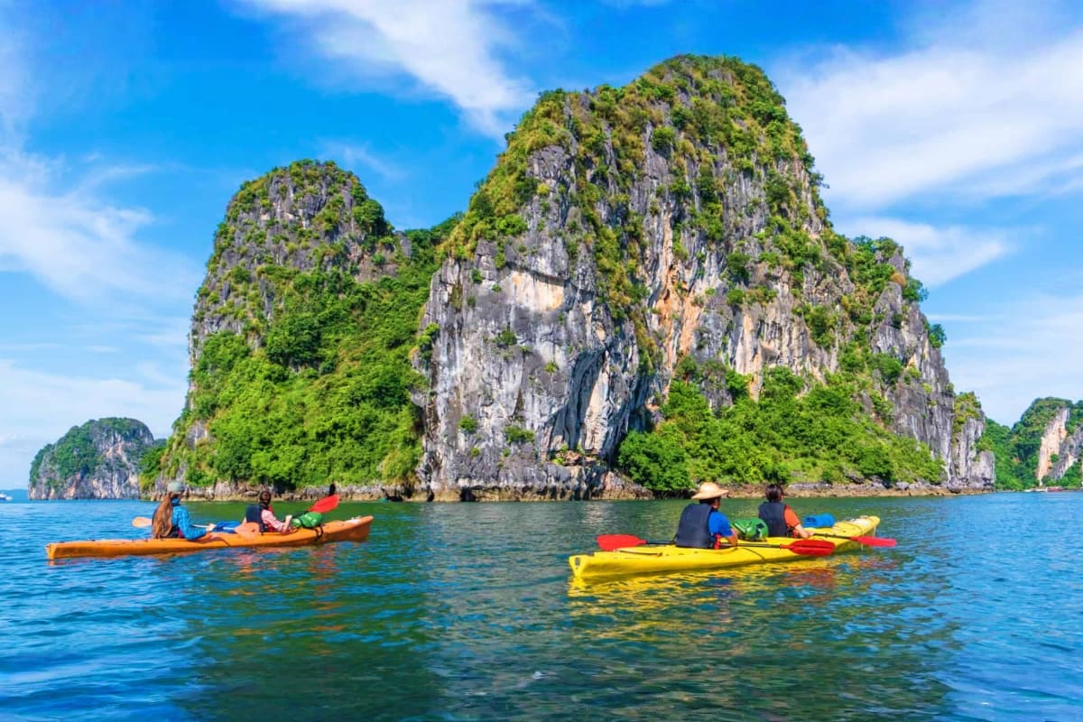 Kayakers paddling colorful kayaks in turquoise waters near towering limestone karst islands covered in green vegetation under