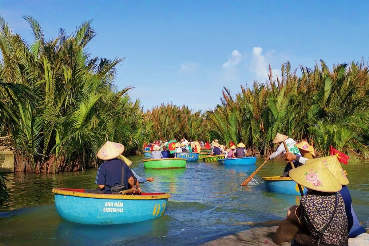 Tourists in traditional conical hats rowing colorful boats through palm-lined waterways in Hoi An, Vietnam