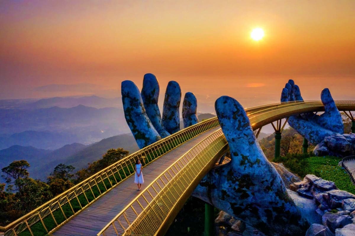 Golden Bridge with giant blue stone hands at sunset in Da Nang, Vietnam, with mountains and mist in background