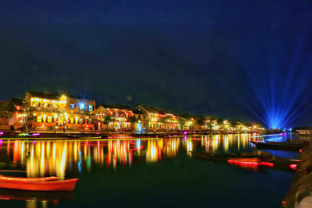 Hoi An ancient town illuminated at night with colorful lantern lights reflecting in the river and red boats, Vietnam