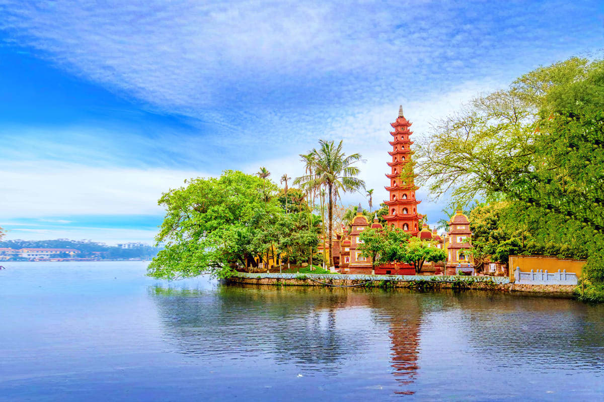 Red Buddhist pagoda reflected in calm lake waters surrounded by green trees and tropical vegetation in Vietnam