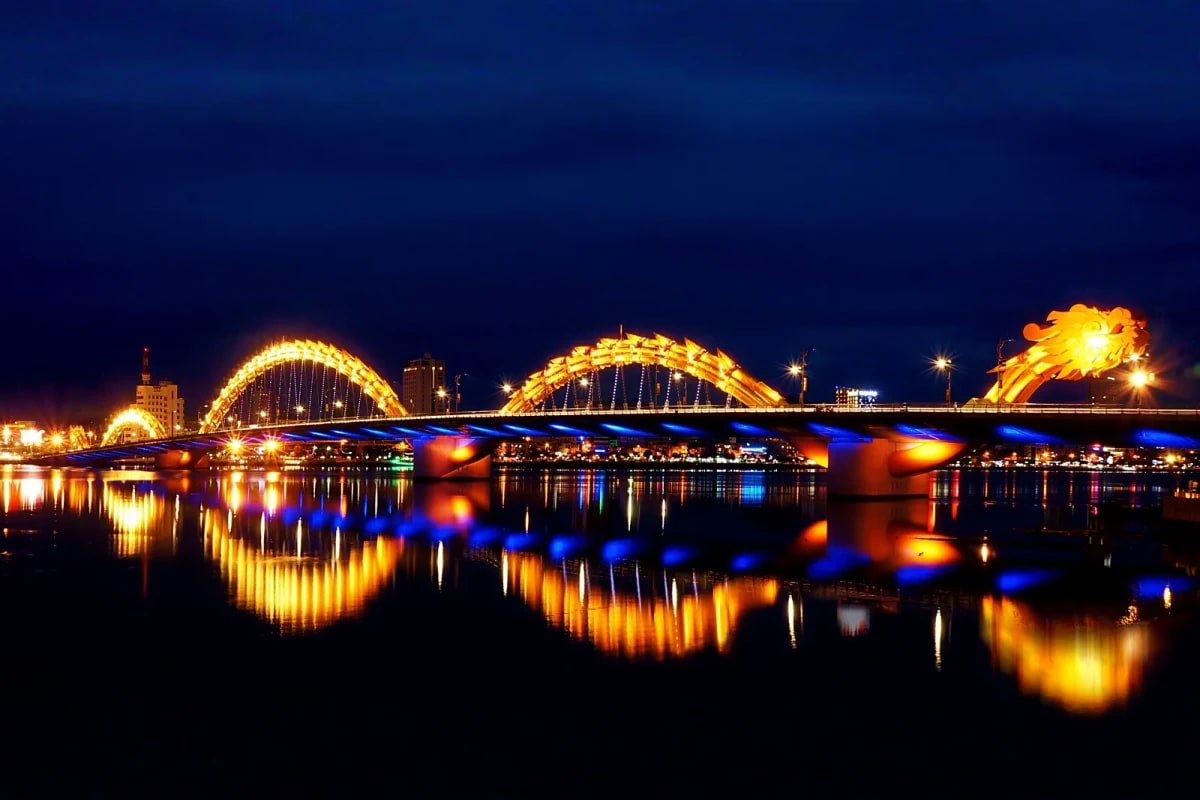 Dragon Bridge illuminated at night with golden and blue lights reflecting in the Han River, Da Nang, Vietnam
