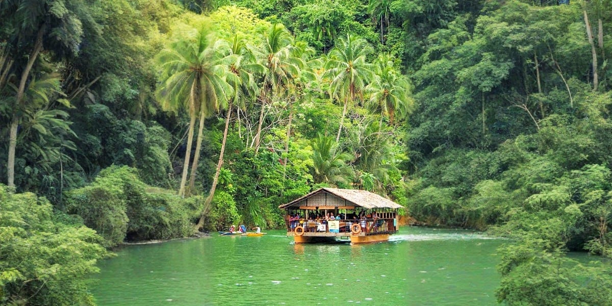Floating bamboo raft bar on turquoise river surrounded by dense tropical forest and palm trees in Bohol, Philippines