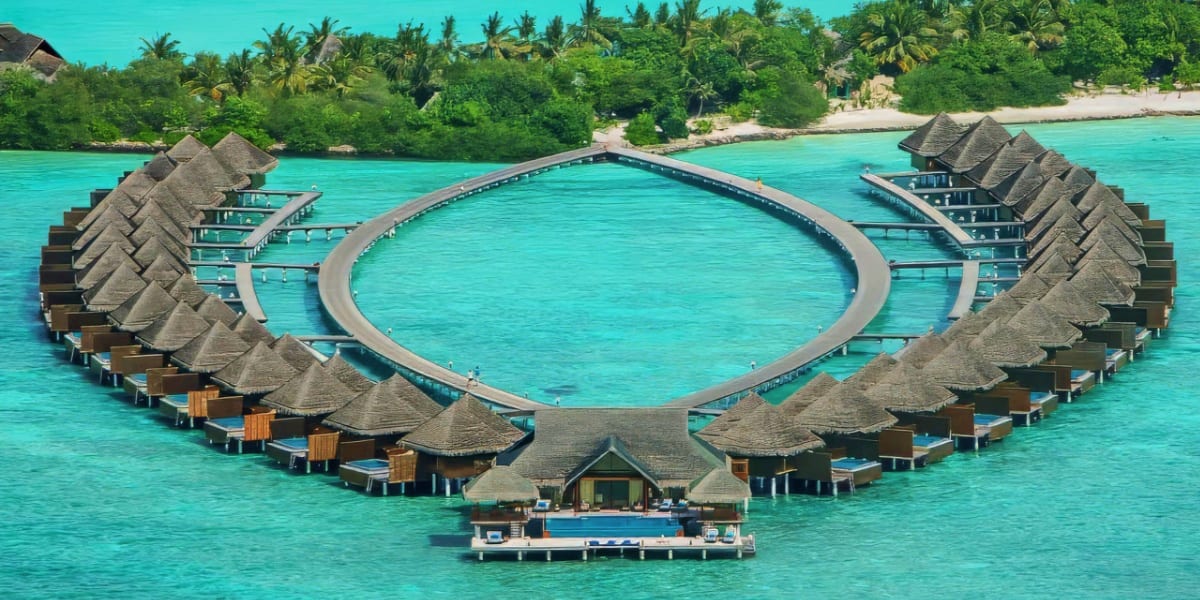 Aerial view of Taj Exotica Resort overwater bungalows arranged in circle around lagoon pool with thatched roofs and turquoise