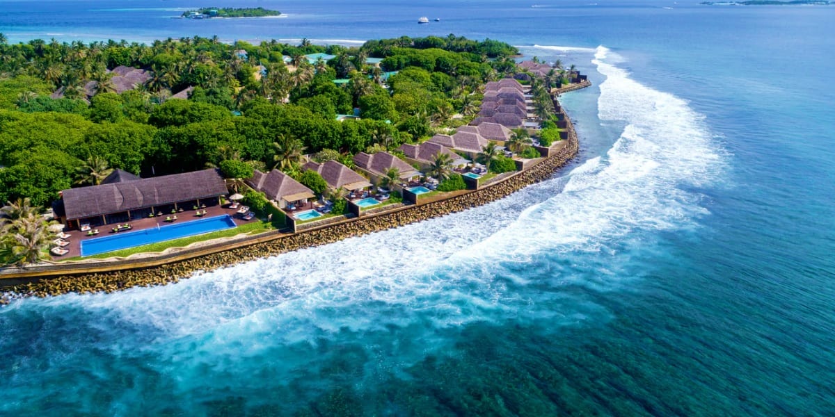 Aerial view of Sheraton Maldives Full Moon Resort with thatched-roof villas, pools, and beach along turquoise ocean waters