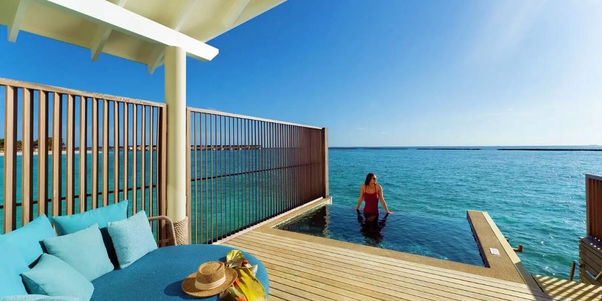 Woman in red dress wading in turquoise water from overwater bungalow deck with ocean views