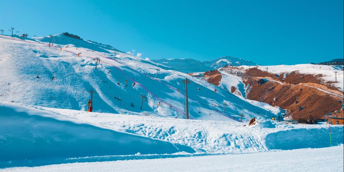 Snow-covered ski slopes with blue markings and ski lifts at an Azerbaijani mountain resort under clear blue sky