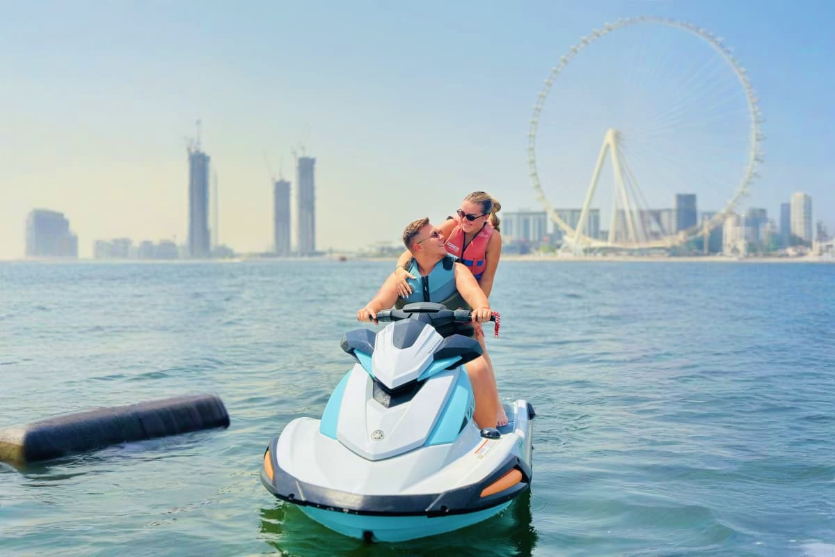 Couple on jet ski in Dubai waters with Ferris wheel and cityscape skyline in background