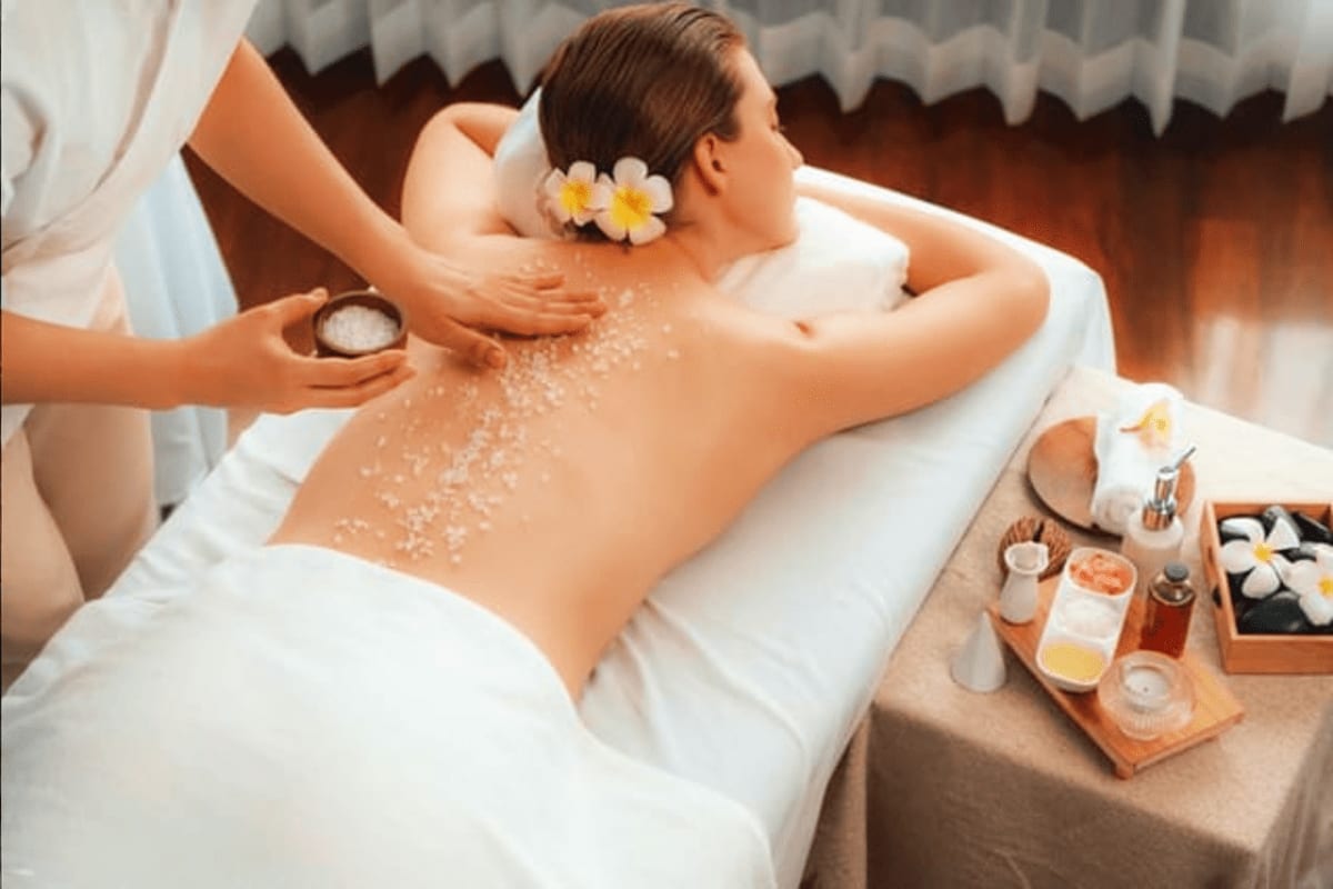 Bella Isa Spa Experience in Boracay Woman receiving back scrub exfoliation treatment at spa with therapist applying salt scrub, flowers in hair, spa products on