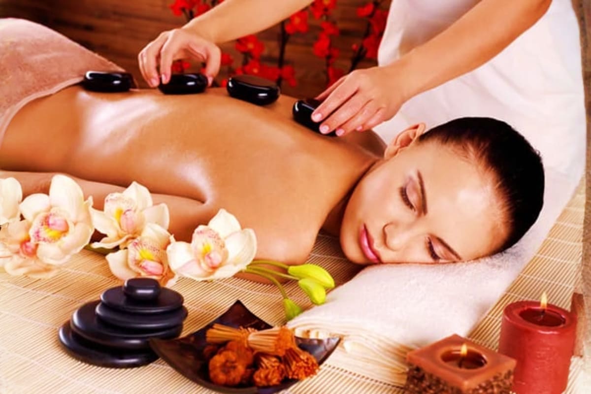 Bella Isa Spa Experience in Boracay Woman receiving hot stone massage therapy on back at spa with orchids, candles, and aromatherapy oils