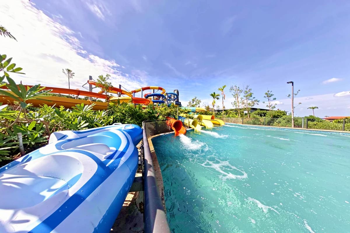 Water slides and pool at SplashMania Water Park with colorful red and blue slides, tropical landscaping, and clear turquoise