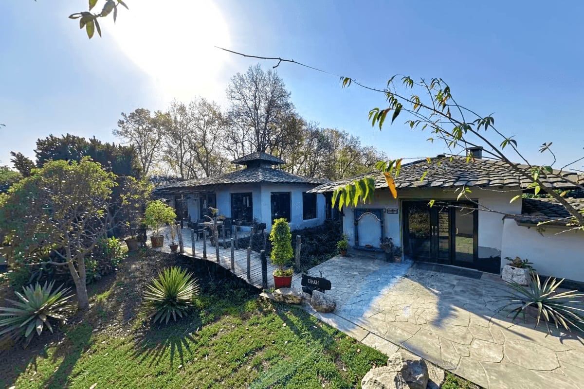White and blue traditional house with slate roof in a village setting, surrounded by green trees and vegetation near Jim Corb