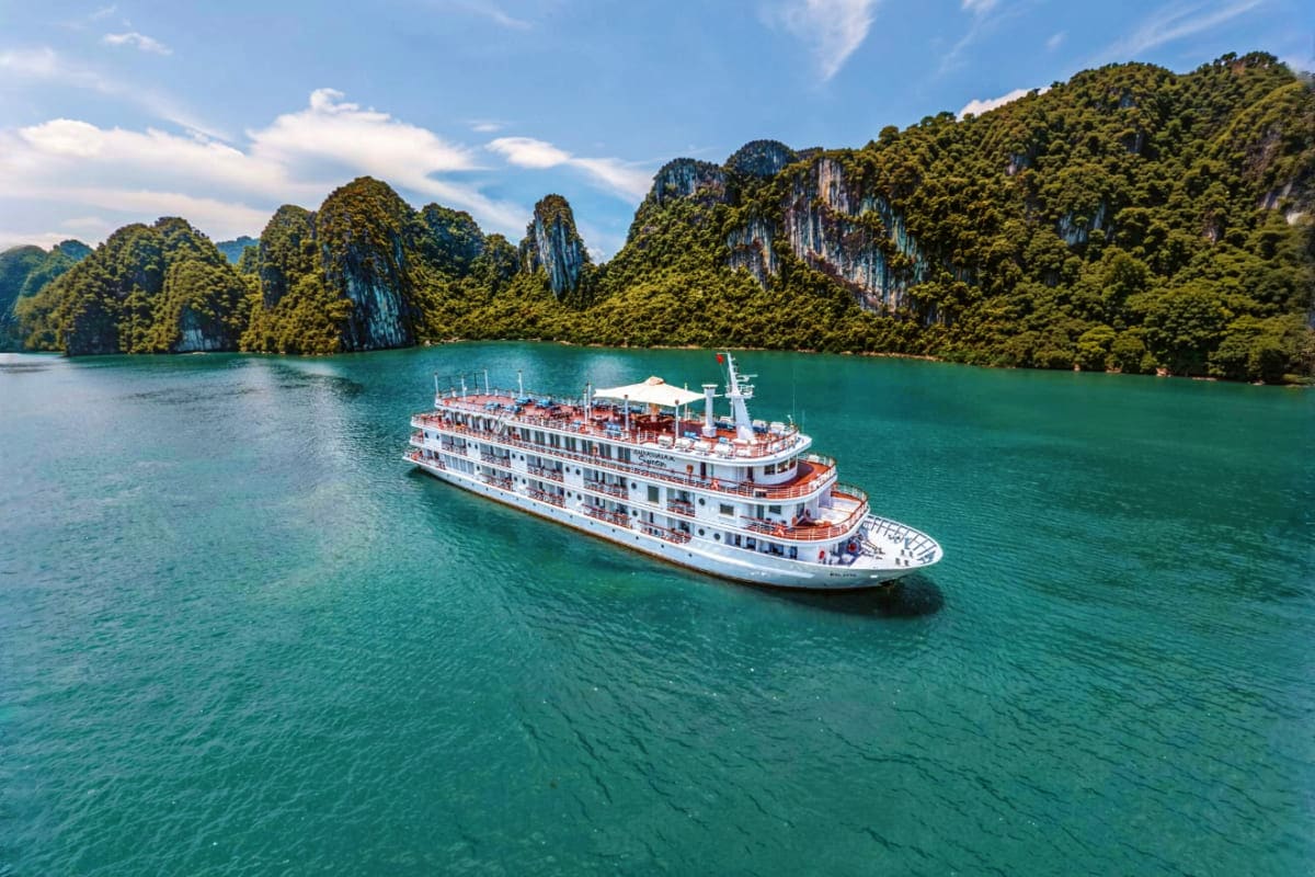 Luxury cruise ship anchored in turquoise waters surrounded by towering limestone karst cliffs covered in dense green vegetati