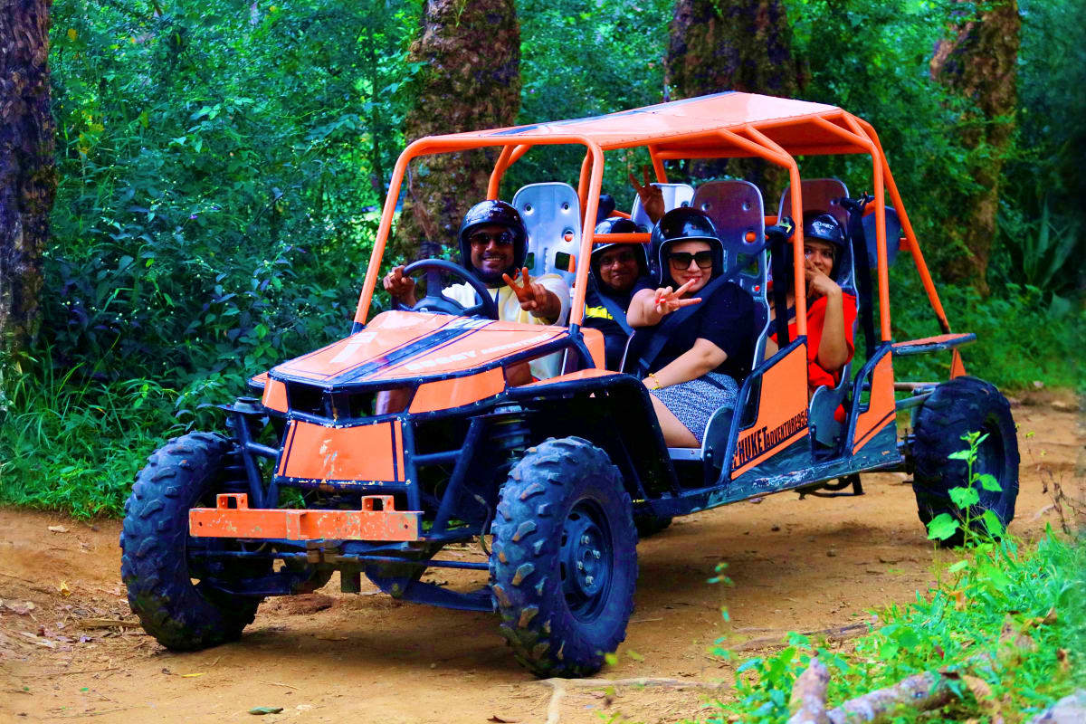 Group of tourists riding orange and blue buggy on dirt trail through lush green forest during Phuket ATV tour