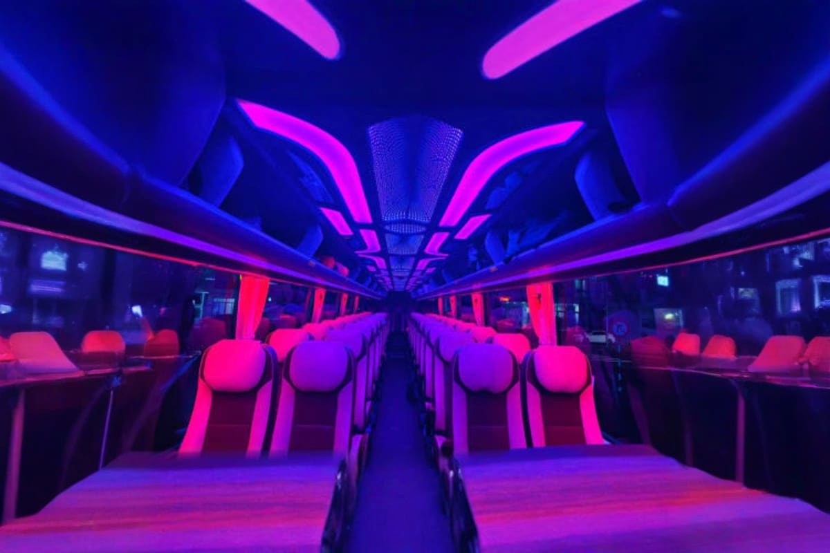 Ho Chi Minh Midnight Airport Pickup Interior of a coach bus with neon pink and blue lighting, empty red seats lining both sides, and fluorescent ceiling lights c