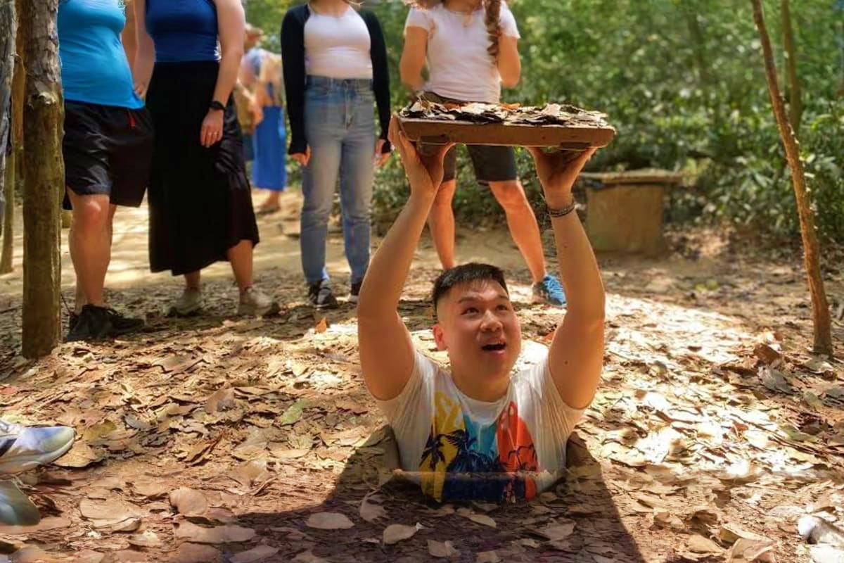 Child emerging from underground tunnel at Cu Chi Tunnels with visitors watching, Vietnam war historic site demonstration