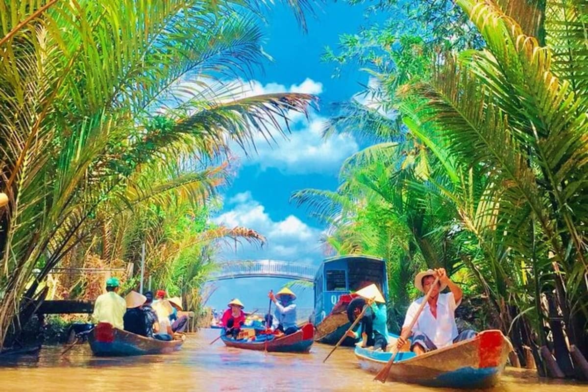 Cu Chi And Mekong Full Day Tour Tourists in traditional wooden boats navigating through palm-lined waterway in the Mekong Delta with blue sky overhead