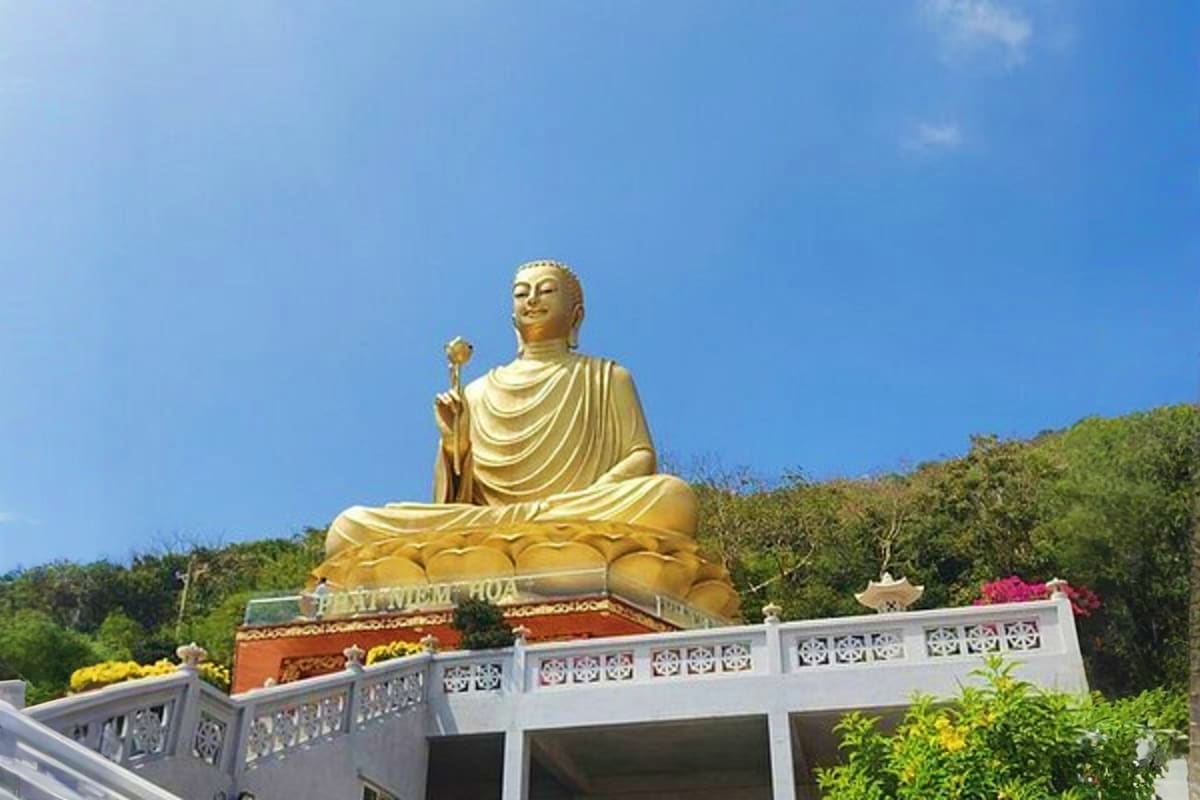 Vung Tau Day Trip Large golden Buddha statue seated on lotus pedestal at Vung Tau temple with clear blue sky and surrounding vegetation