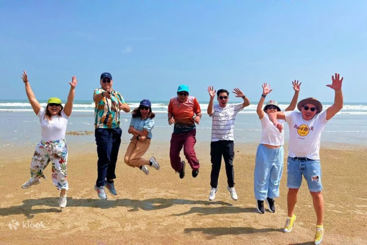 Vung Tau Day Trip Group of eight tourists jumping on sandy beach with ocean and blue sky in background at Vung Tau