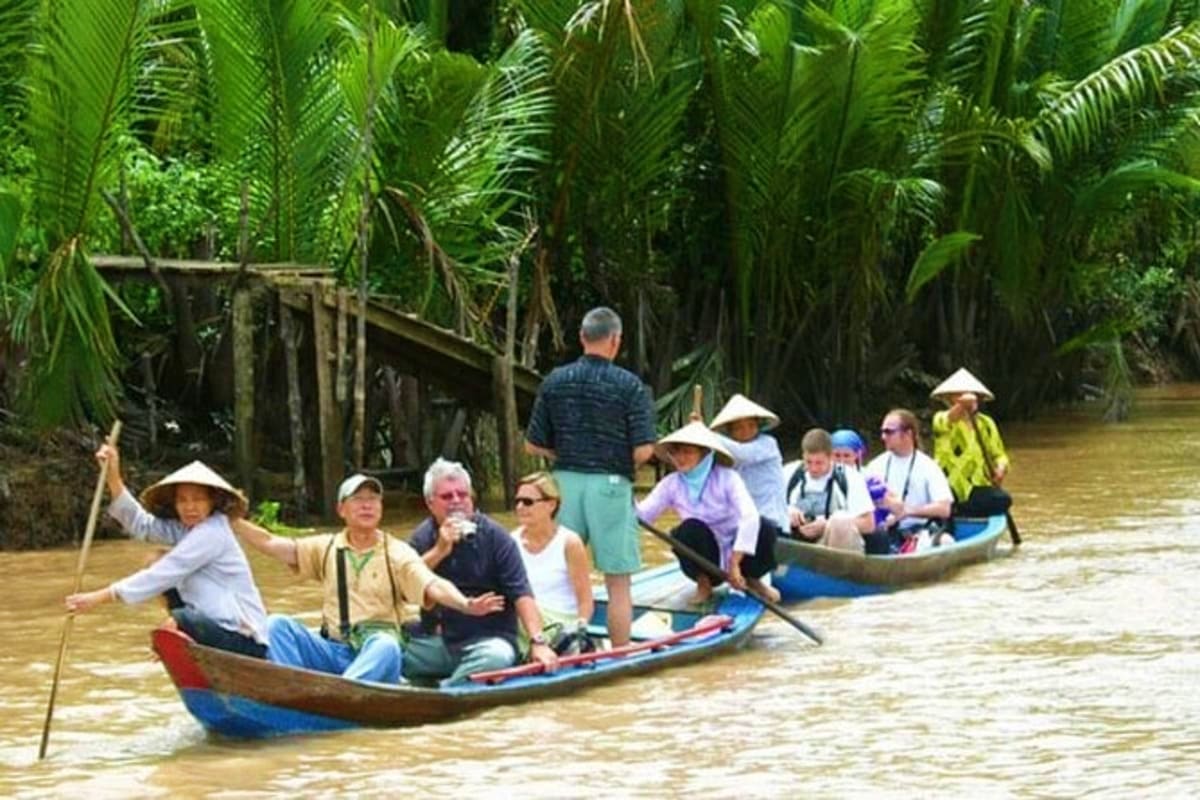 Mekong - Cai Be Tan Phong Island Sharing Tour Tourists in traditional conical hats rowing wooden boats through palm-lined waterway in Mekong Delta