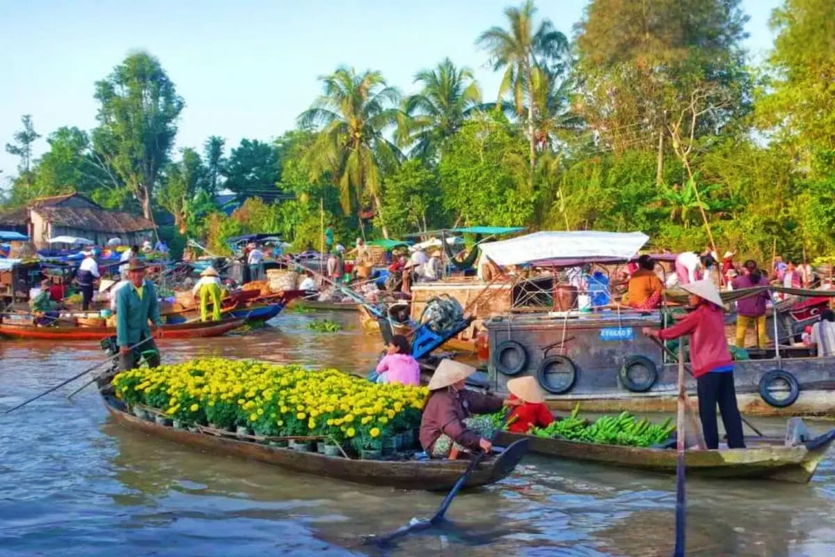 Mekong - Cai Be Tan Phong Island Sharing Tour Floating market boats loaded with yellow flowers and produce on the Mekong Delta waterway with vendors and palm trees in back