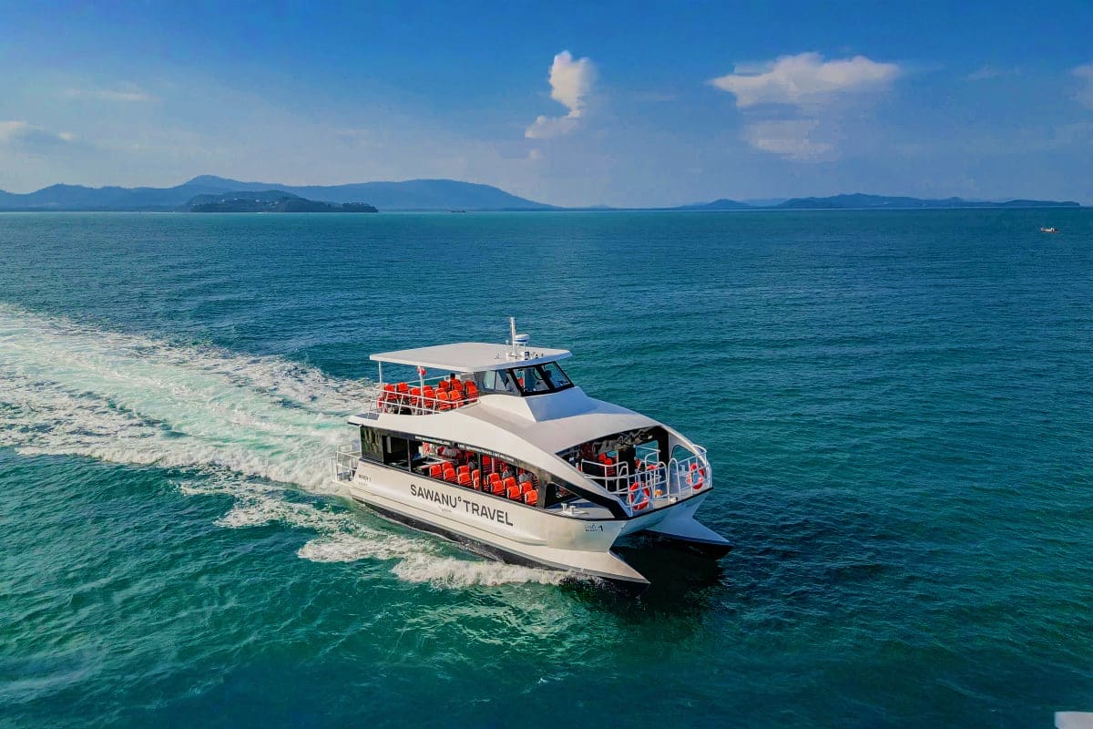 White and black Sawanu Travel speedboat with red seating approaching turquoise waters near tropical islands under blue sky