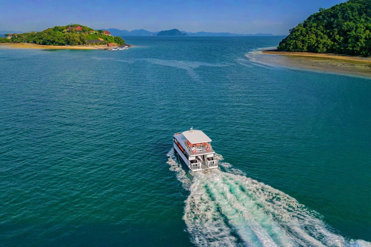 Passenger ferry boat traveling toward forested islands in turquoise Andaman Sea waters with mountains in distant background