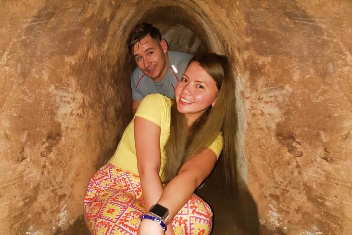 Two tourists smiling inside a narrow underground tunnel at Cu Chi Tunnels historical site