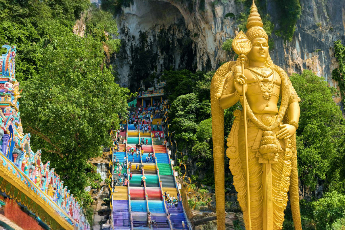 Genting Highlands Tour with Awana Cable Car and Batu Caves Visit Giant golden statue of Hindu deity at Batu Caves entrance with colorful steps and limestone cave in background, Malaysia